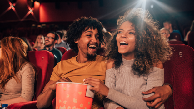 Young man and woman laughing together and sharing popcorn in a cinema