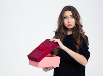 Portrait of a sad woman standing with opened gift box isolated on a white background and looking at camera