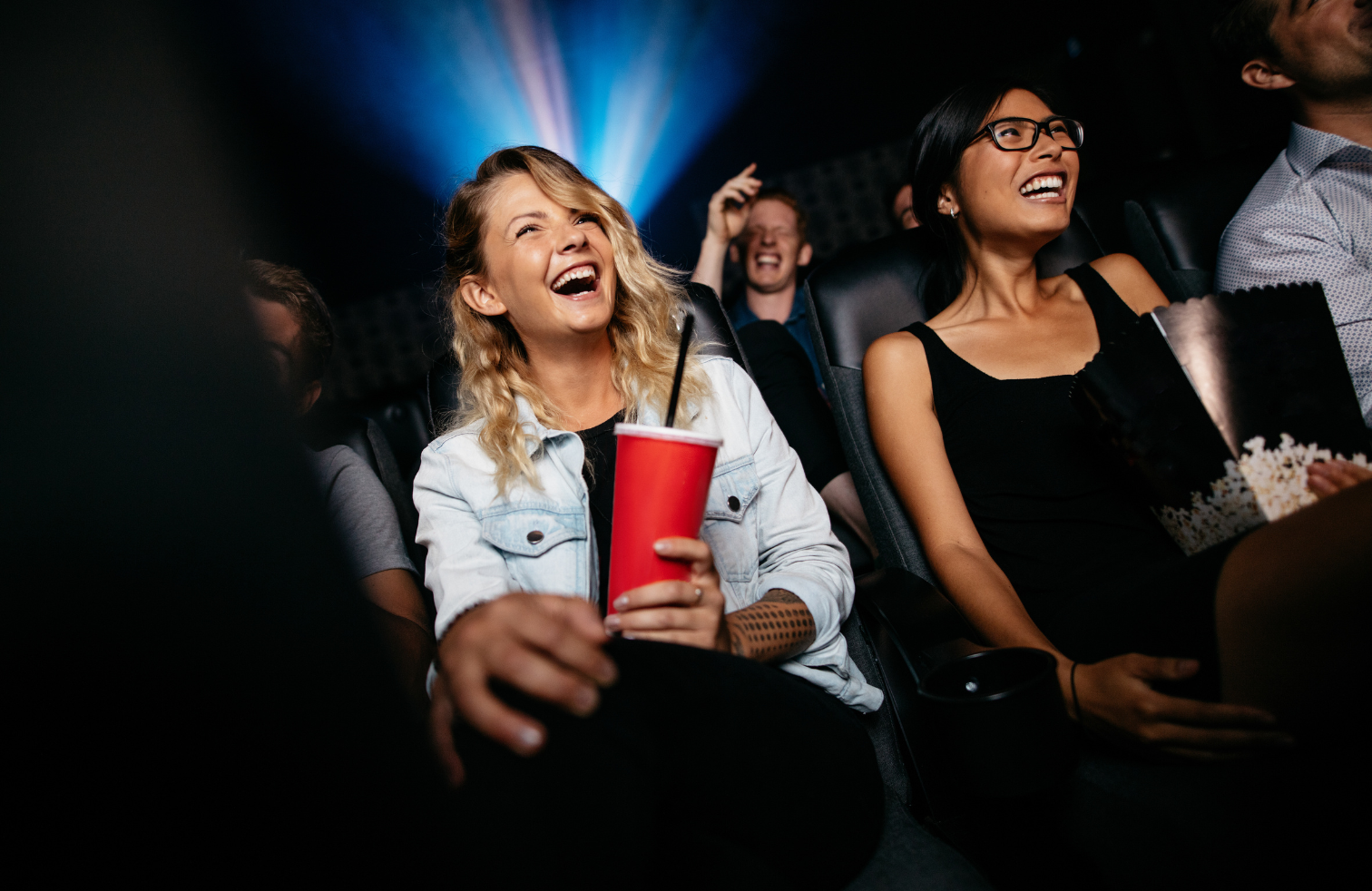 Young lady holding soft drinks cup in the cinema, laughing.